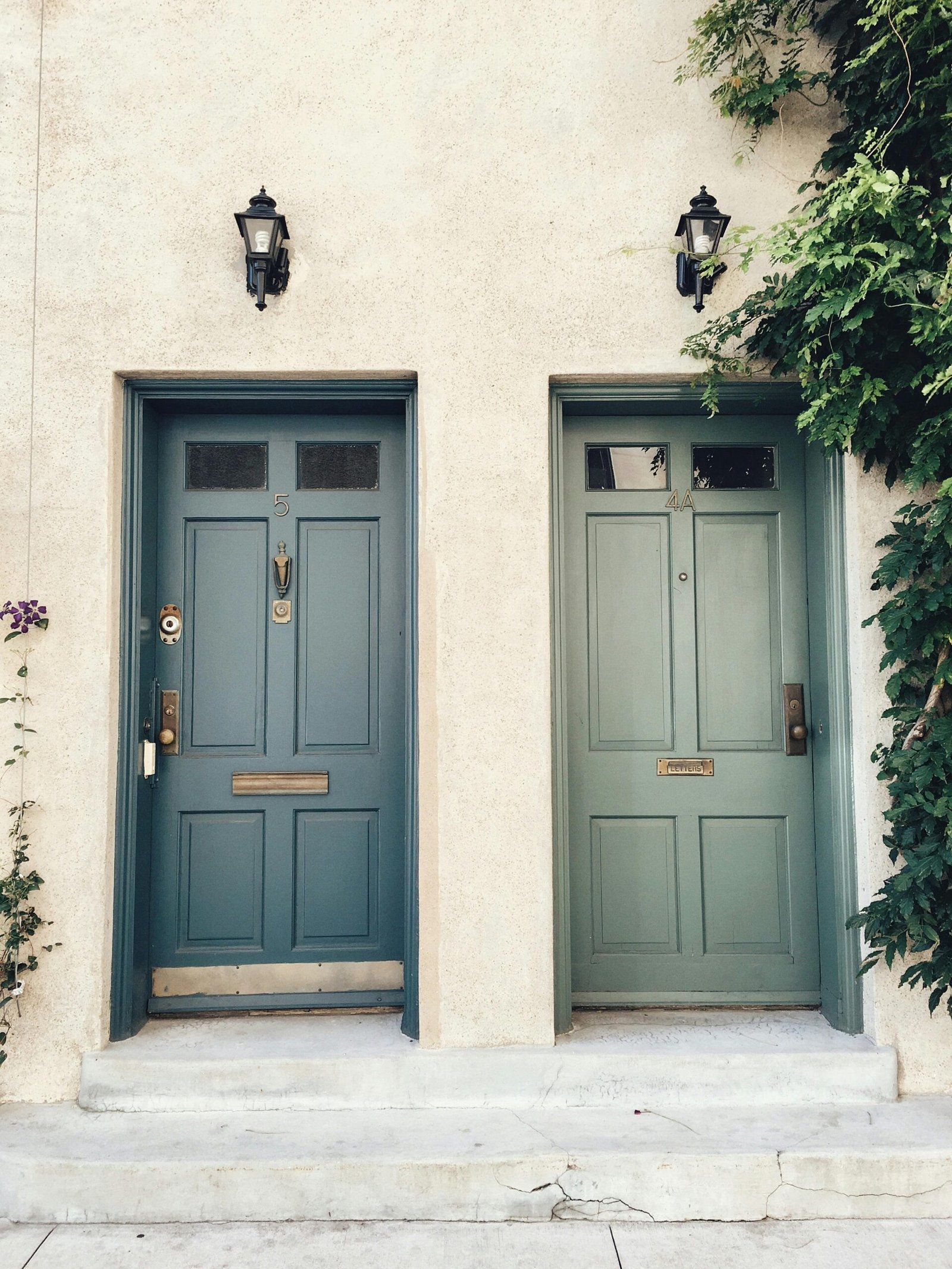 Twin green doors with classic lanterns and ivy on a beige facade.