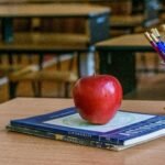 Red apple on books with stationery in a classroom, symbolizing education and knowledge.