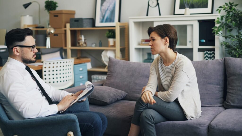 A therapist consults with a client during a counseling session on a sofa in an office setting.
