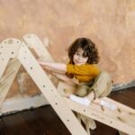 A joyful child with curly hair playing indoors on a wooden ladder toy.