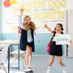 Two excited schoolgirls in uniforms joyfully celebrate back to school indoors.