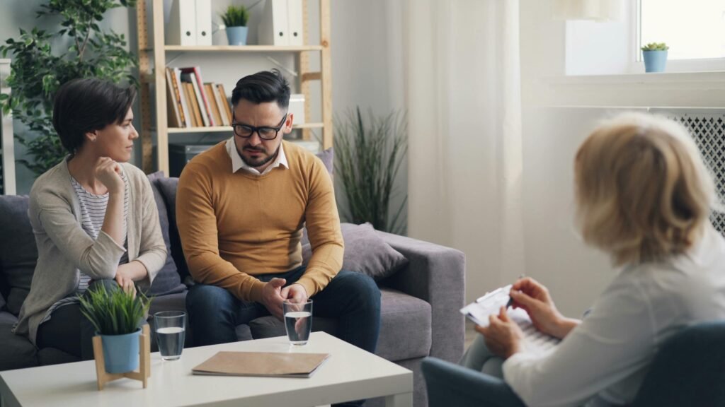 A couple engaged in a counseling session with a therapist in a cozy room.