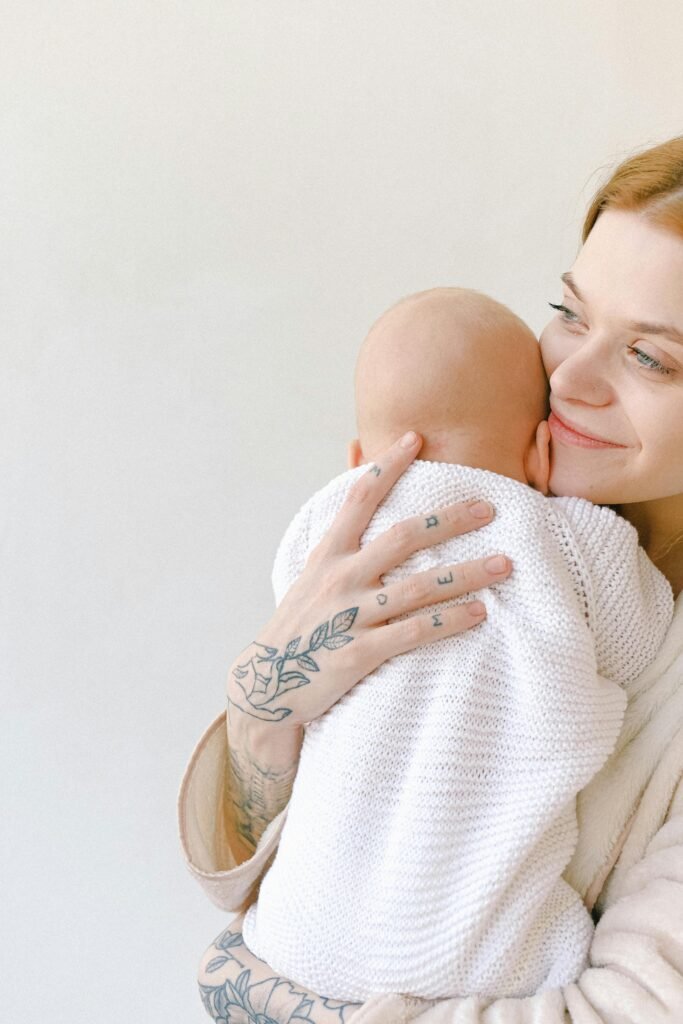 A mother lovingly holds her baby, showcasing her tattooed hand and maternal affection.