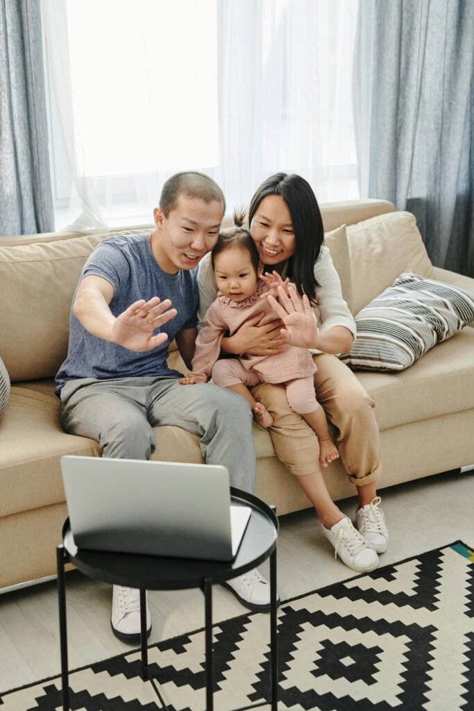 Smiling family waving at laptop during video chat in living room setting.